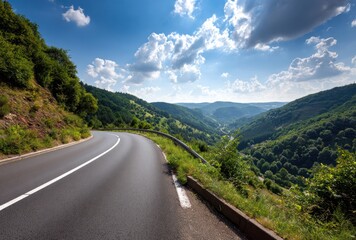 Naklejka premium Scenic view of a winding asphalt road snaking through lush green hills under a bright blue sky dotted with puffy white clouds on a sunny day