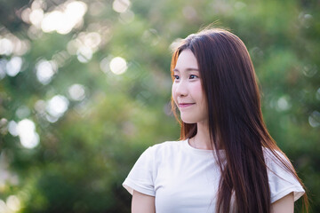 Naklejka premium Young woman with long hair smiles gently while standing outdoors, surrounded by blurred green background