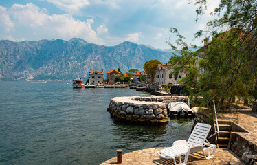 Stone buildings, houses and boat moorings at Donji Stoliv on the south shore of the Bay of Kotor in Montenegro. Sailing boats in the bay, mountains in background. 