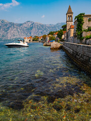 The Catholic church of Saint Basil and a row of stone buildings at Donji Stoliv on the Bay of Kotor shoreline in Montenegro. Mountains rise in background. 