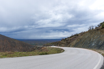 a curved asphalt road downwards through the cliffs under the cloudy sky 