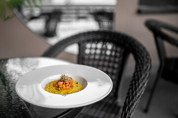 Gourmet saffron risotto served on a white plate, garnished with tomato relish and herbs, photographed outdoors on a glass table with soft background blur.