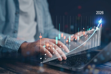 Businessman using laptop with virtual holographic graph projecting positive growth trend for year 2026, indicating increasing profits and successful investment strategy