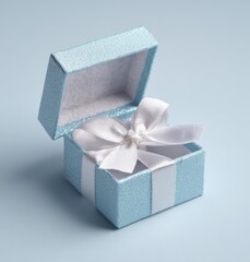 Open, small blue box with a white ribbon bow inside. Pastel background. Textured box. Bow is neat and tidy, prominent against the blue interior