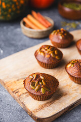 Autumn pumpkin cupcakes or baked muffins with fresh pumpkin and pumpkin seeds for Thanksgiving day on wooden cutting board
