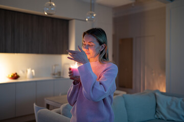Serene middle aged woman enjoy smelling lighted scented aromatic candle in glass filling cozy home...