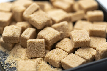 Organic brown sugar cubes in black bowl close up natural sweetener textured surface healthy ingredient rustic kitchen soft focus delicious and inviting
