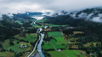 Fototapeta premium Experience the breathtaking beauty of Stryn, Norway, with rolling green hills, meandering rivers, and dramatic clouds. The vibrant landscape invites exploration, perfect for nature lovers.