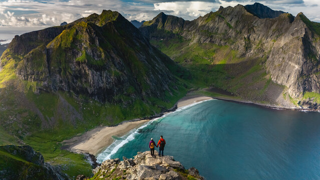 Hikers enjoy the dramatic landscapes along the Ryten Kvalvika Beach Trail, surrounded by towering mountains and pristine beaches. The vibrant colors of nature create a captivating atmosphere.