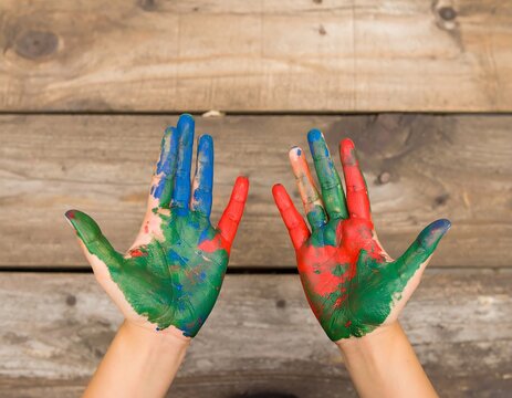 Two hands painted with vibrant colors on rustic wood