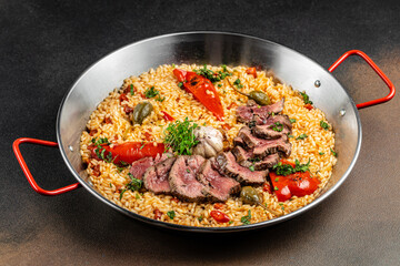 Paella with sliced beef, rice, red peppers, garlic, and capers in a traditional pan. top view