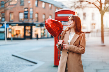 Woman holding heart-shaped balloon in a city street during daylight, showcasing joy and celebration...