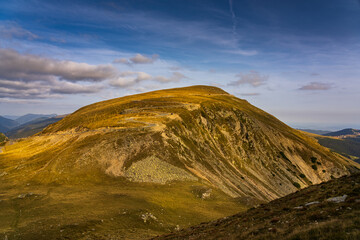 A solo traveler experiences a breathtaking autumn day in the wild Carpathian Mountains, near Lake Galcescu, in the Parang Mountains of Romania, where vibrant fall colors meet rugged peaks