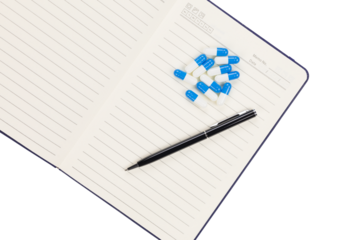 Open notebook with blue and white capsules and black pen symbolizing medical reminder and healthcare concept.