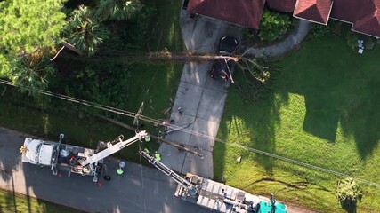 Utility services fixing damaged power lines after hurricane in Florida. Workers using bucket trucks to repair blown down electrical wires at residential home.