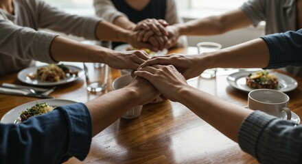 Hands joined in a circle before a meal at a wooden table  