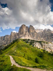 A scenic summer path winds through the Dolomites at Passo Giau, Italy, surrounded by lush greenery and towering peaks, offering breathtaking views of the majestic alpine landscape