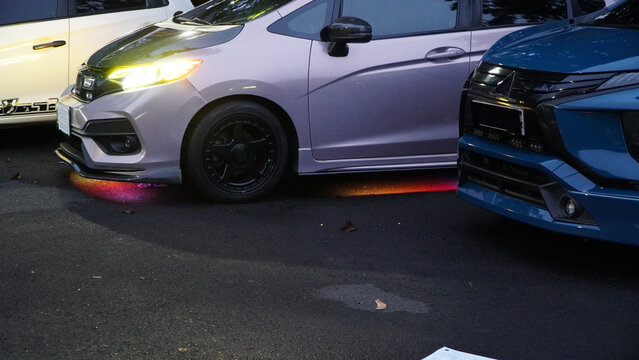 Wonosobo, Indonesia - 30 August 2025: Modified cars with colorful RGB underglow lights parked at night car meet, vibrant neon ground lighting.