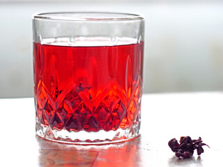  A Glass of Red Hibiscus Tea with Dried Flowers on the Side
