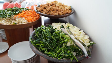 buffet station with fresh vegetables and tofu in wooden bowls, leafy greens, carrots, sprouts,...