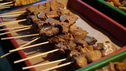 grilled chicken liver skewers arranged in red-bordered tray lined with parchment paper, golden-brown surface and seasoning suggest savory street food in casual prep setting