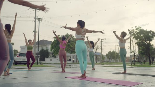 Group of women performing Tadasana (Mountain Pose) with arms raised during a morning yoga session outdoors.