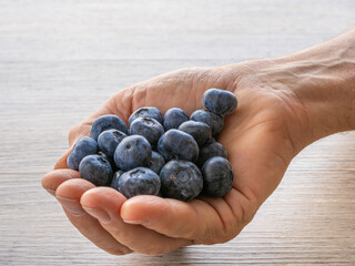 Fresh ripe blueberries in a man's hand on wooden table, close-up healthy food concept.
