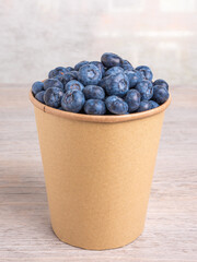 Fresh ripe blueberries in eco paper cup on wooden table, healthy organic food concept.
