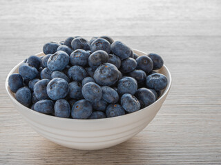 Fresh ripe blueberries in a white bowl on wooden table, healthy organic fruit rich in antioxidants and vitamins.
