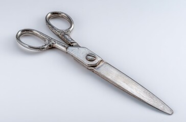 Obraz premium Elegant, silver scissors lie open on a bright white surface, showing the detailed handle design and the slightly worn, straight blades