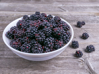 Organic blackberries in white bowl on wooden background, fresh fruit harvest concept.
