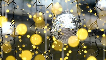 A close-up of a sparkling silver disco ball surrounded by glowing string lights and golden bokeh, evoking celebration and festivity.