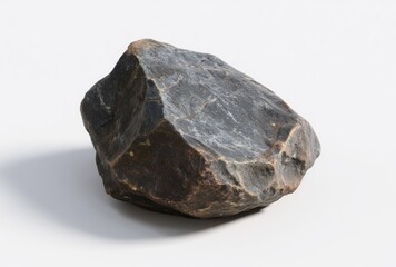 A dark grey, irregularly shaped rock with textured surfaces sits on a white surface, casting a soft shadow to the lower left