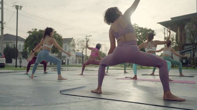 Diverse group of women performing Reverse Warrior (Viparita Virabhadrasana) during a sunrise yoga class in an open-air setting.