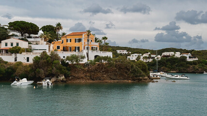 Fototapeta premium Coastal villa with orange walls and white details overlooking a calm bay. Menorca, Mahon