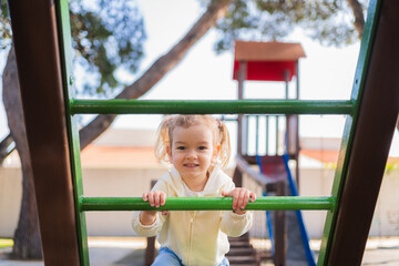 Fototapeta premium Cute toddler girl playing on monkey bars at playground