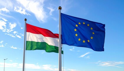 Hungary and European Union flags flying side by side against blue sky with clouds, symbolizing national and regional unity.