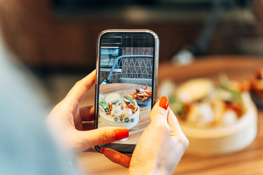 Close-up of a woman photographing gourmet Asian food with a smartphone