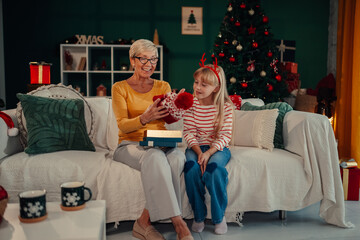 Obraz premium Grandmother giving christmas gift to granddaughter on sofa