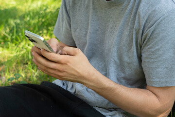 A person sits in a lush garden under a tree, focused on their smartphone. The vibrant greenery emphasizes the contrast between nature and digital engagement.
