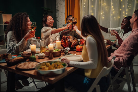 Friends toasting during thanksgiving dinner with roasted turkey and candles