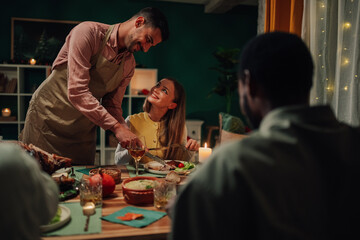 Man serving food to woman during festive dinner with friends