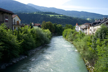 Serene river flowing through lush greenery and charming houses with mountains in the background, perfect for nature lovers