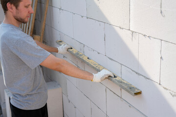 A construction worker carefully checks the alignment of building blocks with a level tool while...