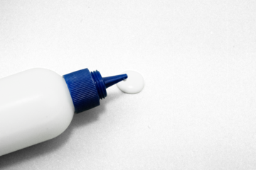 Close up of white glue bottle with blue cap dispensing adhesive on textured surface