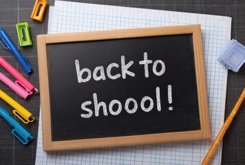 Slate blackboard with "back to shoooool!" message, pen, sharpener and open notebook on a gray surface, top view