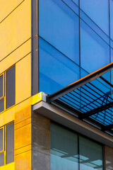 Modern architectural detail of yellow building with glass windows and reflections