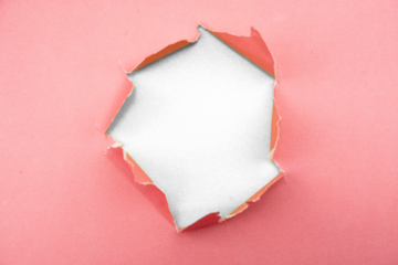 Torn pink paper abstract close up revealing blackness behind texture