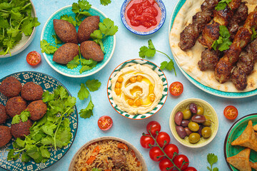 Top view of a vibrant table filled with lebanese dishes and mezze, featuring meat kebabs, falafel, kibbeh, hummus, sambousek, rice, olives. Middle eastern or Arab dishes