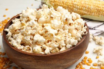 Tasty popcorn and corn kernels on white table, closeup